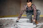 Instalator układa rury ogrzewania podłogowego na izolacji w budowanym domu